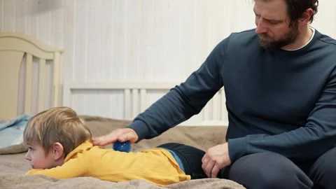 Father using a spiky massage ball for son to relieve muscle tension, aid Stock Footage 307773468
