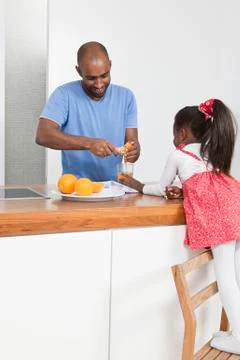 A father using a wooden juice extractor while his daughter watches Stock Photos