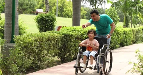 Father walking around park with disabled son in wheelchair Stock Footage 249044371