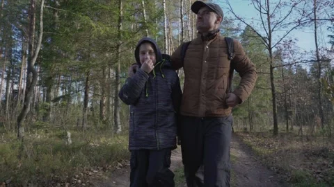 Father walks along path in forest hugging son by shoulder Stock Footage 238475651