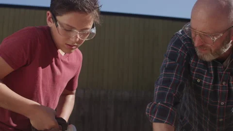 A father watches his son using a circular saw to cut a piece of wood Stock-Footage 132540550