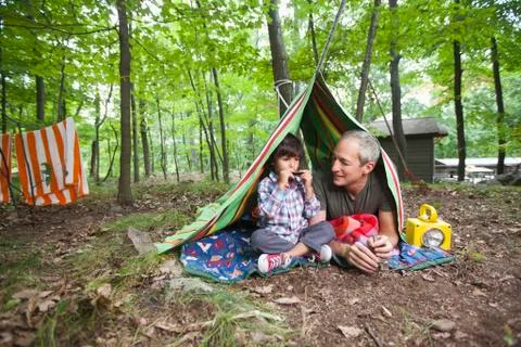 Father watching son playing harmonica in blanket fort Stock Photos