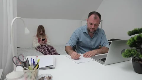 Father working diligently at desk while daughter sits on bed, engrossed in Stock-Footage 317266187