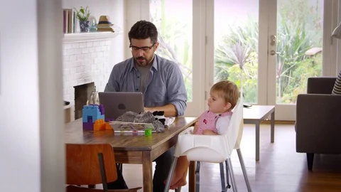 Father Working From Home On Laptop As Son Plays With Toys Stock Footage