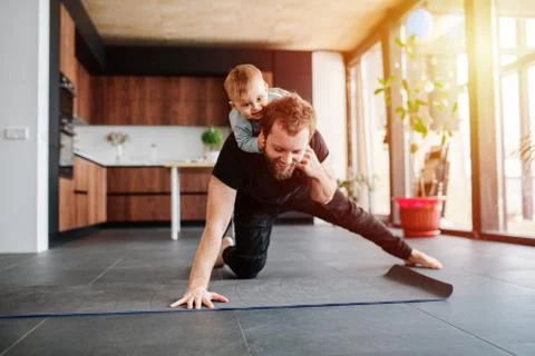 Father working out, doing single arm plank with his jolly baby riding on him Stock Photos