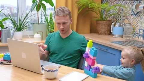 Father works remotely in the kitchen on a laptop, daughter little child pla.. Stock Footage 321116079