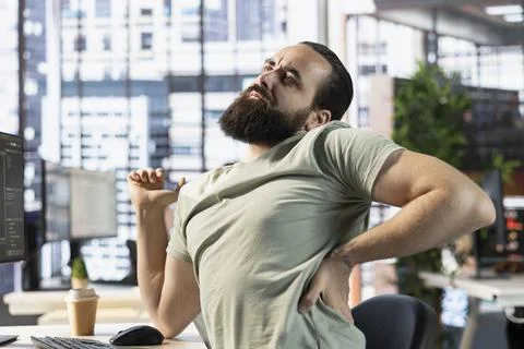 Fatigued man with sore back while analyzing data on computer Stock Photos