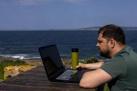 Favorite work. The most beautiful work. A man behind a laptop by the ocean. Stock Photos
