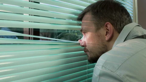 FBI agent looking and observing through jalousie in his safe house Stock Footage 97687096