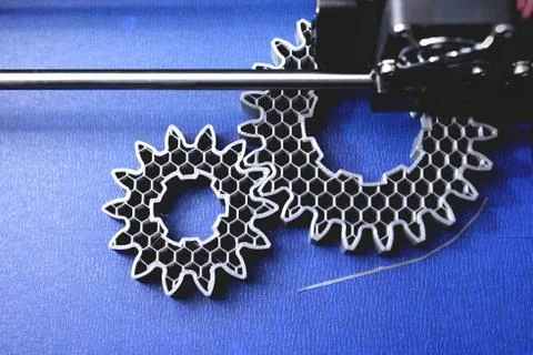 FDM 3D-printer manufacturing spur gears from silver-gray filament on blue pri Stock Photos