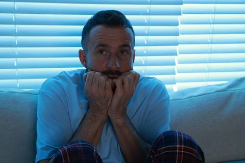 Fear of darkness. Scared man on couch in dark room Stockfoto's