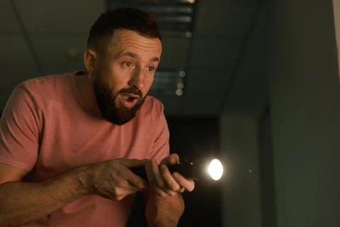 Fear of darkness. Scared man with flashlight indoors at night, space for text Stock Photos