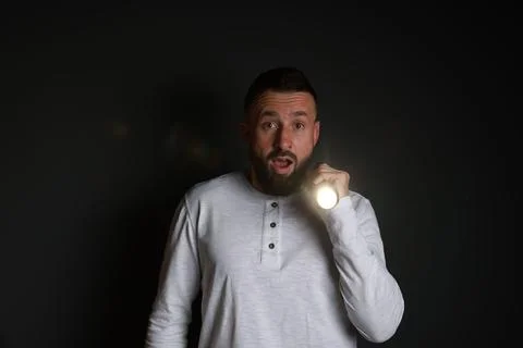 Fear of darkness. Scared man with flashlight on black background Stock Photos