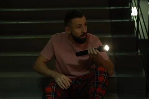 Fear of darkness. Scared man with flashlight indoors at night Stock Photos