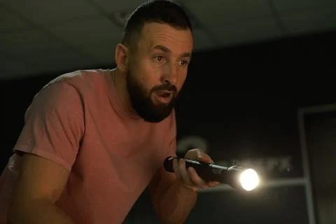 Fear of darkness. Scared man with flashlight indoors at night Stock Photos