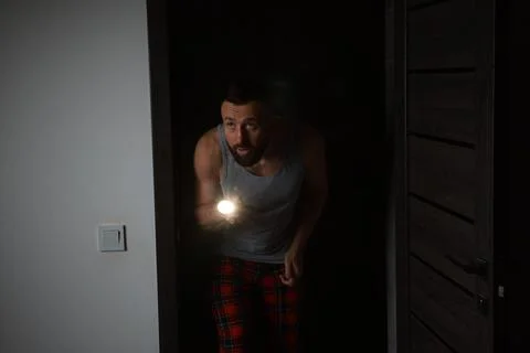 Fear of darkness. Scared man with flashlight in room at night 스톡 사진