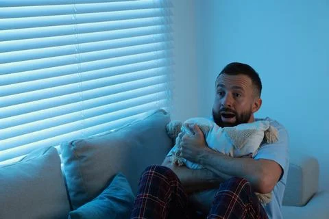 Fear of darkness. Scared man hugging pillow on couch in dark room, space fo.. Fotos de archivo