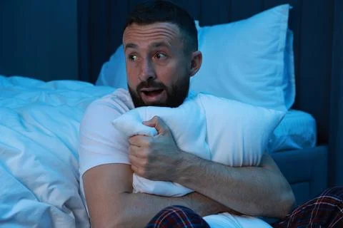Fear of darkness. Scared man hugging pillow in bedroom at night Fotos de archivo