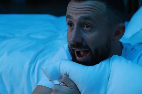 Fear of darkness. Scared man hugging pillow in bedroom at night Stock Photos