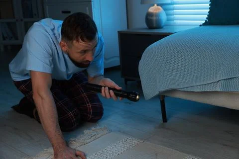 Fear of darkness. Scared man looking under bed with flashlight indoors at nig 写真素材