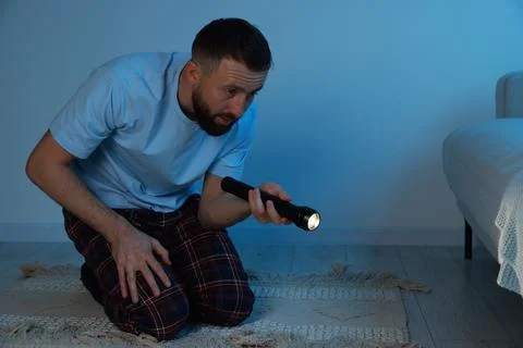 Fear of darkness. Scared man looking under bed with flashlight indoors at nig Stock Photos