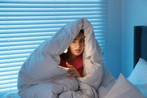 Fear of darkness. Scared young with blanket and flashlight on bed indoors a.. Fotos de archivo