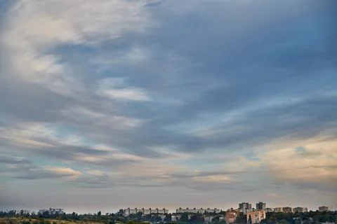 Feather clouds in the evening light on the blue sky over the fields and house Stock Photos