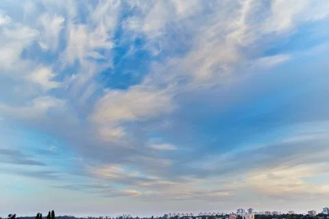 Feather clouds in the evening light on the blue sky over the city Stock Photos