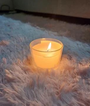 Featured object scented candle with a soft glow under a shaggy rug creating a Stock Photos