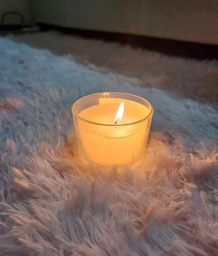 Featured object scented candle under a furry rug. Stock Photos