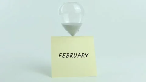 February written on yellow sticky note placed on hourglass on white Stock Footage 313482623