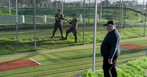 Feeder tossing balls, pitching machine firing, batter swinging bat in cage for Stock Footage 334840958