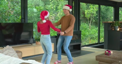 Feeling holiday cheer, diverse couple wearing Santa hats grabbing hands, dancing Stock Footage 337159784