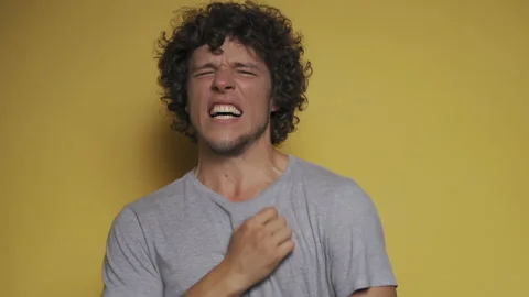 Feeling pain young guy with long curly hair twists in pain isolated against a Stock Footage 143617832