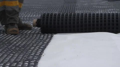 Feet of construction worker unrolling roll of geogrid for roadbed reinforcement Video stock 158051225