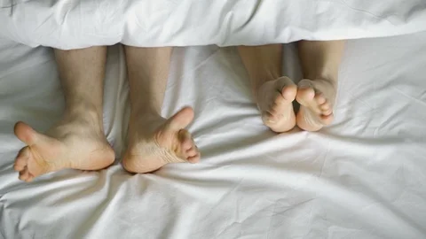 Feet dancing under a white blanket, on a white bed, top view.4k Stock Footage 106538568