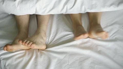 Feet dancing under a white blanket, on a white bed, top view.4k Stock Footage 106539064