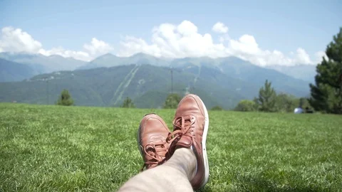 Feet of a guy while relaxing on lawn against firs, blue sky, clouds and 스톡 동영상 114961992