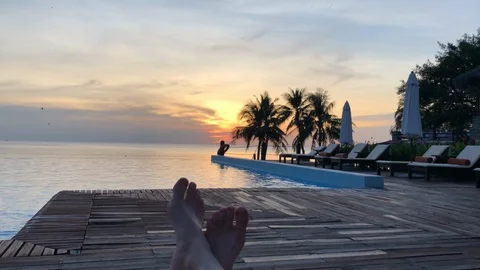 Feet at infinity pool by the ocean at sunset with palm trees in background Stock Footage 107575441