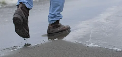 Feet of man in jeans and boots on sandy beach near sea in slow motion Stock Footage 140625053