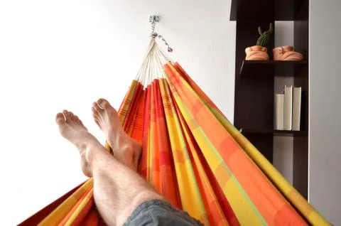 Feet of man lying down in bright hammock attached to indoor wall in house Stock Photos