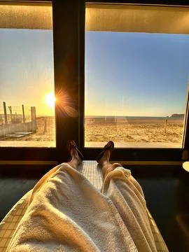Feet point of view from bed looking at sunrise beach through window Stock Photos