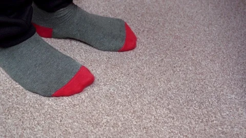 Feet in red-grey socks on a light brown carpet rub against each other. Standing Stock-Footage 124575447