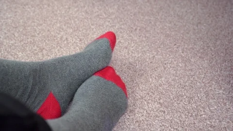 Feet in red-grey socks on a light brown carpet rub against each other Stock-Footage 124579345