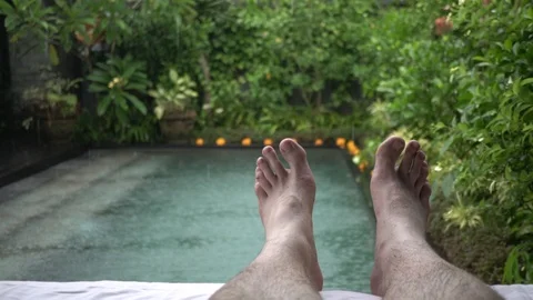 Feet of a resting young man on the background of the pool in the rain in Bali. Stock Footage 104439103