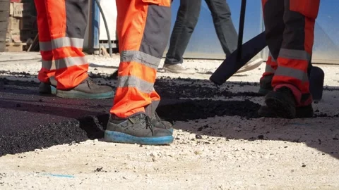 Feet of unknown construction workers spread asphalt on the ground Stock Footage 251889851