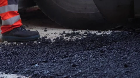 Feet of unknown construction workers spread asphalt on the ground Видео 251889858