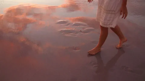 Feet walking across wet beach sand with reflection of sunset sky Stock Footage