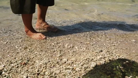 A feet walking barefoot along a sandy shore as gentle ocean waves splash Stock Footage 342733219