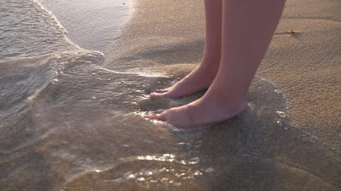 Feet in Water Waves on Sandy Beach with Sea Foam on Coast. Woman Stood in Sand Stock Footage 94491642
